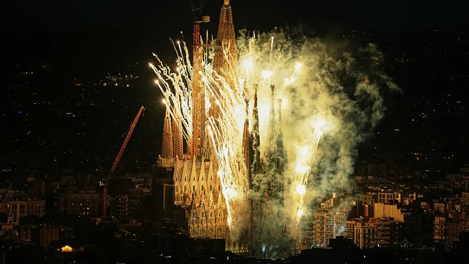 Sagrada Família illuminata di notte con fuochi d’artificio e colonne di fumo giallo sopra Barcellona.